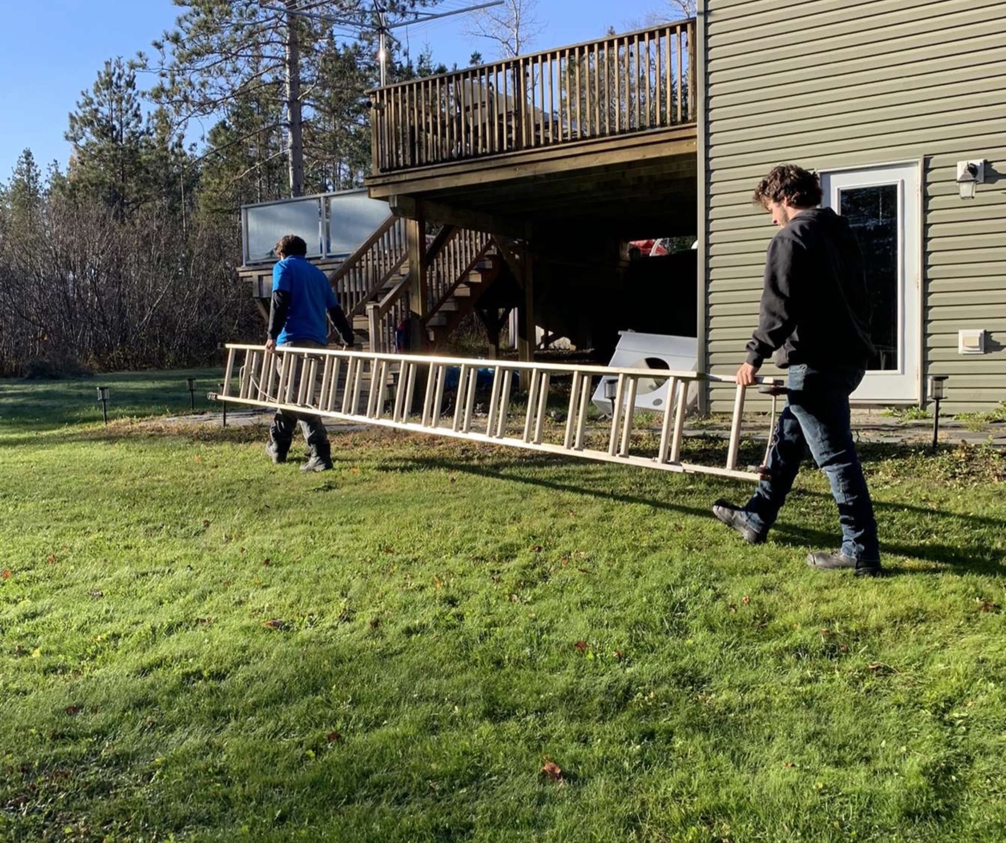 Two Wash Wizards crew members carrying a ladder across a lawn