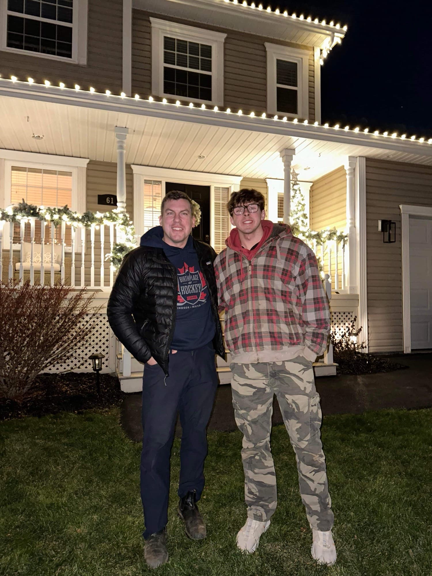 Two of the Wash Wizards crew in front of a house lit in warm white roofline lights