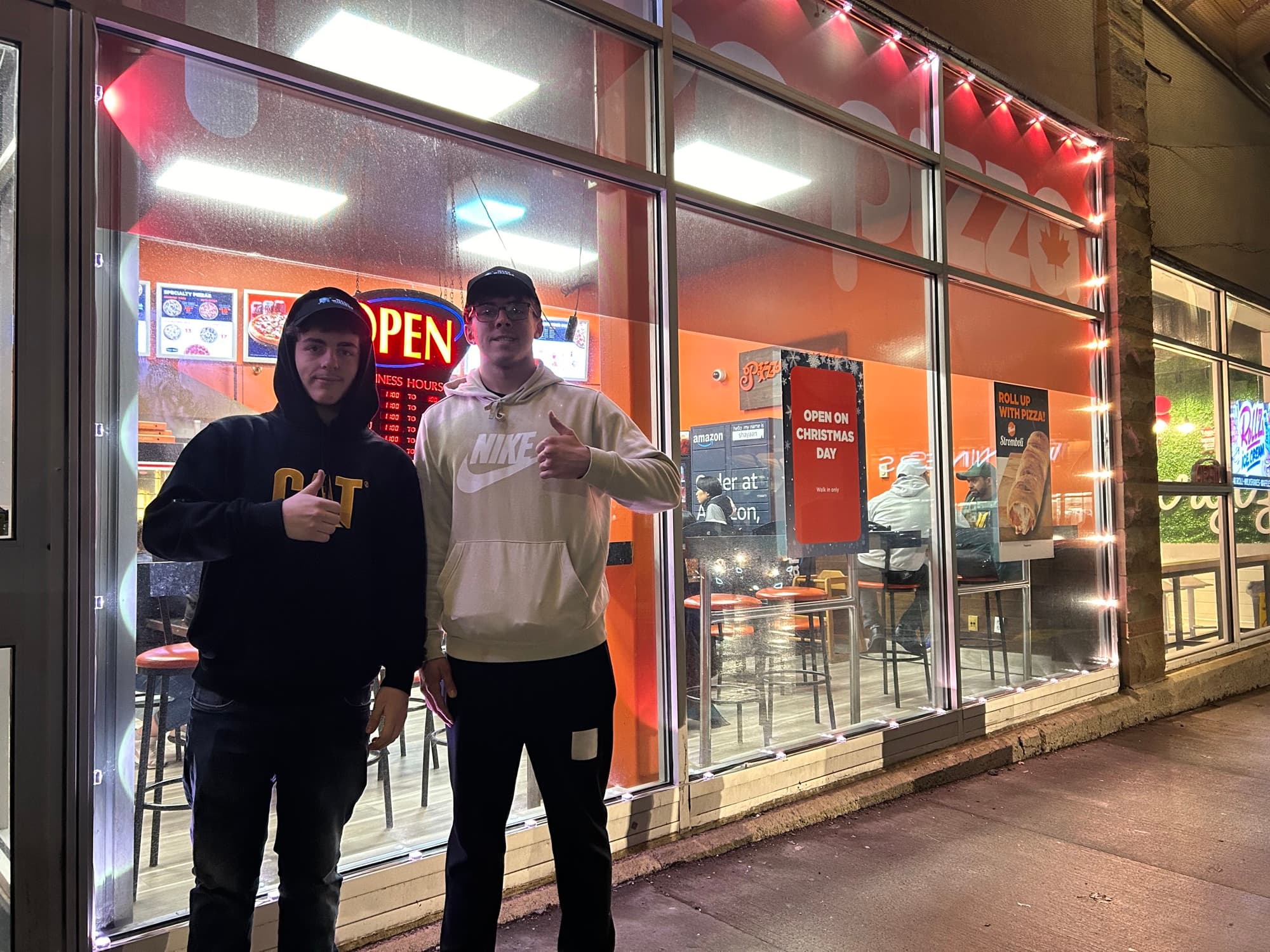 Two of the Wash Wizards crew outside Picasso Pizza, its storefront lit along the top