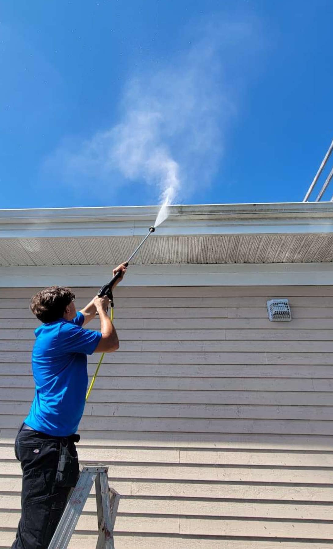 A Wash Wizards crew member on a ladder power washing a soffit
